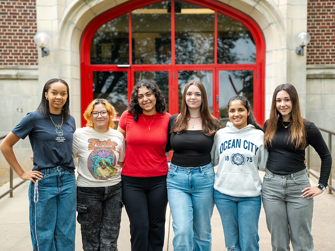 A group of six college students stands in front of a red door